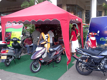 Electric scooters displayed under a red canopy at a public exhibition